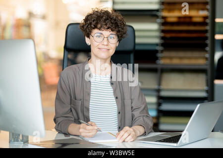 Young confident teacher or office manager making notes by desk Stock Photo
