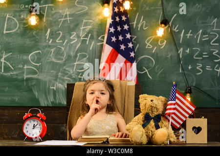 Parents usually put their kids into academic coaching. Teacher helping kids with computers in elementary school on the USA national flag background. Stock Photo