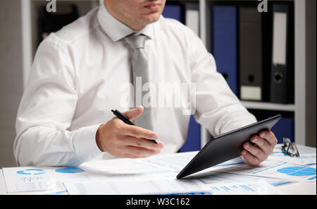 Businessman working with tablet pc, calculating, reading and writing reports. Office employee, table closeup. Business financial accounting concept. Stock Photo