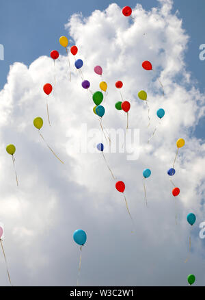 many balloons flying high in the sky with white clouds in the background Stock Photo