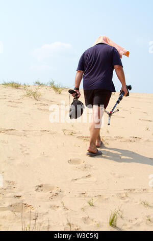 Kharkiv, Ukraine - July 31, 2016: Adult male photographer with a towel on his head from the heat is walking with a camera on a stand in the desert Stock Photo