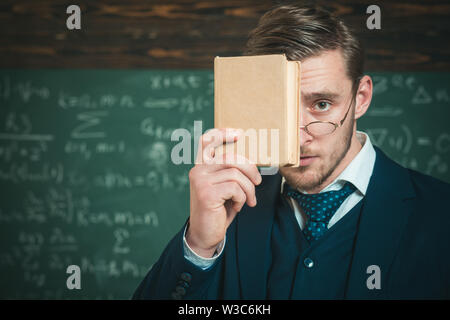 You should remember. Teacher formal wear and glasses looks smart, chalkboard background. Man unshaven holds book in front of face. Teacher insists on Stock Photo