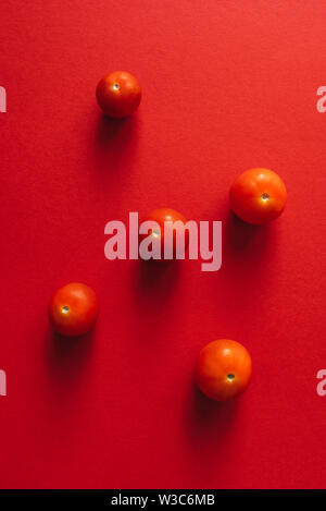 Five cherry tomatoes on a red background. Stock Photo