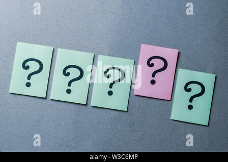 Line of four printed question marks on green paper and one on pink raised above the others in a concept of leadership, diversity and individualism ove Stock Photo