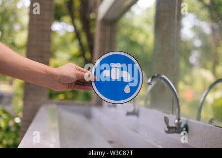 Male hands holding a blue faucet sign with the tap water faucet in the park. Save water and environmental concern concept Stock Photo