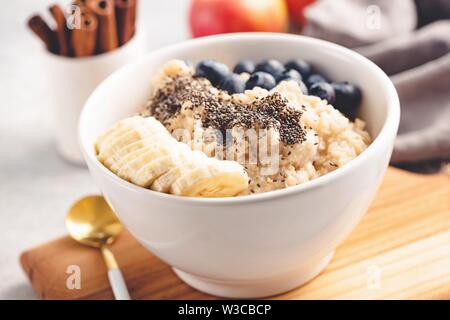Oatmeal porridge with blueberries, banana and chia seeds in bowl. Closeup view, selective focus, toned image. Healthy breakfast food. Concept of clean Stock Photo