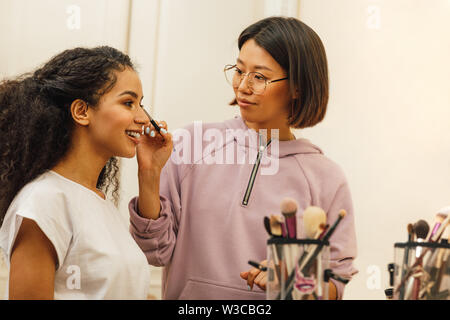Makeup artist applying makeover on a model face in dressing room Stock Photo