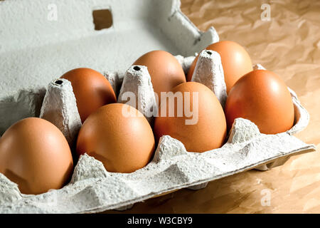 Seven brown chicken eggs in a carton paper packaging on a kitchen table. Eggs for breackfast. Healthy eating and food Ingredients. Stock Photo