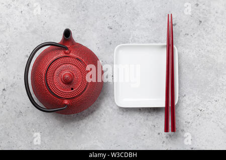 Empty plate, teapot with herbal tea and chopsticks over textured table. Japanese food template. Top view with copy space. Flat lay Stock Photo