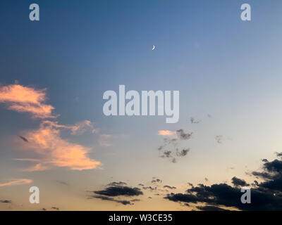 Calm evening sky with moon and dark and pink stratocummulus clouds Stock Photo