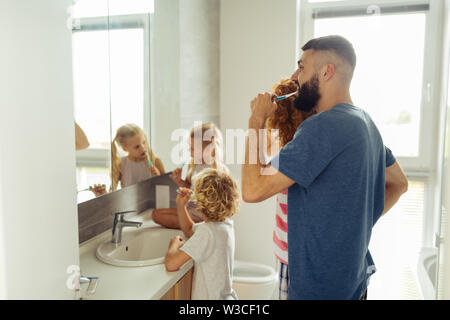 Brushing teeth. Nice bearded man putting a brush in his mouth while brushing teeth together with his family Stock Photo