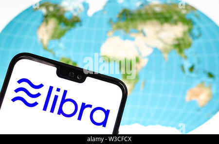 Facebook Libra crypto currency logo on the smartphone and the world map at a laptop screen on the background. Conceptual photo. Stock Photo