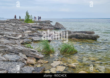 Tourists scramble across the rocks while exploring the rocky shoreline Flowerpot Island Tobermory Ontario. Stock Photo