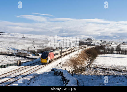 Virgin Trains class 390 pendolino train passing Shap Wells, Cumbria on the west coast mainline in the sunshine and snow Stock Photo