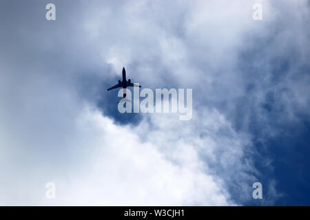 Airplane in the blue sky with white clouds. Commercial plane in a flight close up, bottom view Stock Photo
