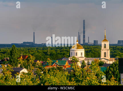 the Church is lit by the sun against the grey of the pipes metallurgical plant Stock Photo