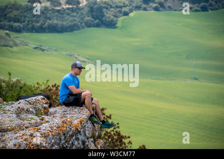 A man sitting on a cliff and overlooking the plains of Ronda, Spain near Acinipo