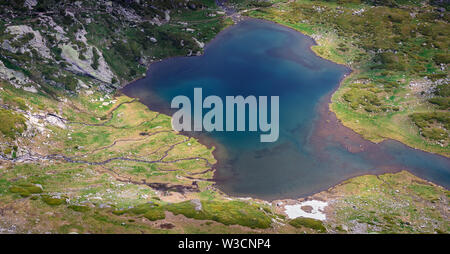 Panorama of the Twin lake on Rila mountain in Bulgaria, it's delta with meandering mountain creeks and sunlit rocky highlands viewed from Lake peak Stock Photo