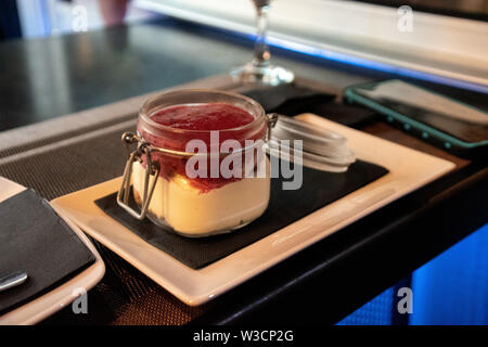 A dessert time cheesecake with a strawberry jam topping served in a glass mason jar