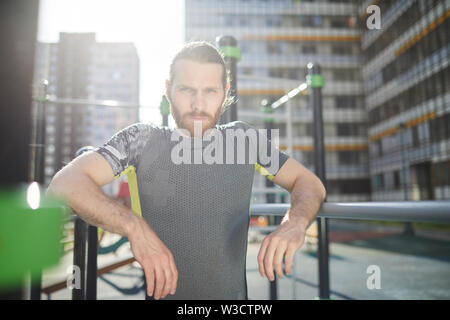 Portrait of serious determined handsome workout athlete with red beard leaning on parallel bars on outdoor ground Stock Photo