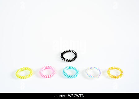 Plastic bracelets of various colors, isolated in a pattern arranged in white background, with a black to be different. Stock Photo