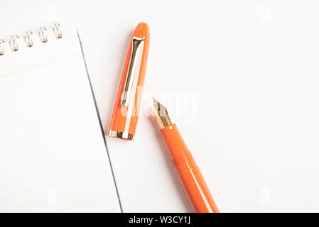 A shiny orange fountain pen together with a spiral-bound ruled notebook. Stock Photo