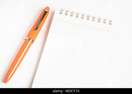 A shiny orange fountain pen together with a spiral-bound ruled notebook. Stock Photo