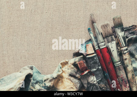 Artist paint brushes, paint tubes closeup on brown linen canvas. Stock Photo