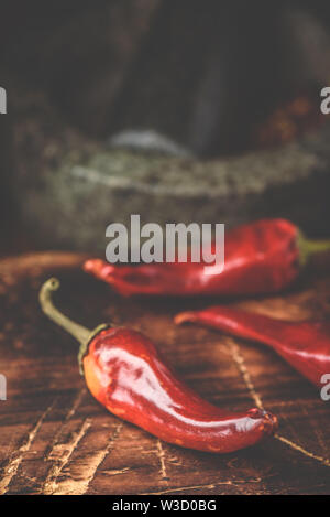 Sun dried red chili peppers on wooden surface with mortar and pestle Stock Photo