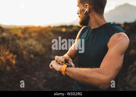 Athletic runner start training on fitness tracker or smart watch and looking forward on horizon. Trail running and active lifestyle concept. Stock Photo