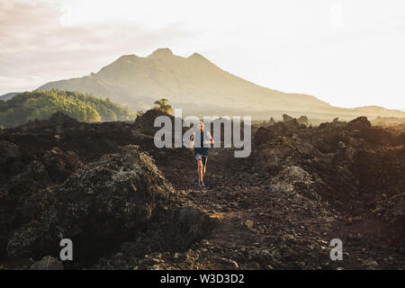 Young athlete man trail running in mountains in the morning. Amazing volcanic landscape of Bali mount Batur on background. Healthy lifestyle concept. Stock Photo