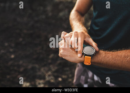 Young athletic man using fitness tracker or smart watch before run training outdoors. Close-up photo with dark background. Stock Photo