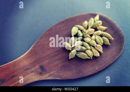 Dry cardamom seeds on a brown wooden spatula. Natural food spices and seasonings. Tasty eating. Close-up. Stock Photo