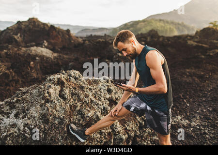 Young man stretching before running and looking in phone. Synchronisation music with headphones. Stock Photo