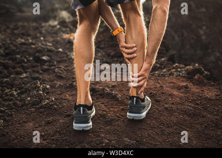 Male runner holding injured calf muscle and suffering with pain. Sprain ligament while running outdoors. View from the back close-up. Stock Photo