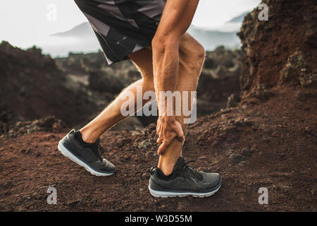 Male runner holding injured calf muscle and suffering with pain. Sprain ligament while running outdoors. Close-up legs view. Stock Photo