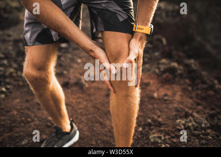 Knee injury on running outdoors. Man holding knee by hands close-up and suffering with pain. Sprain ligament or meniscus problem. Stock Photo