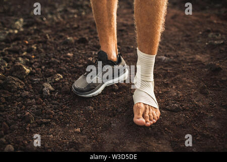 Man's ankle in compression bandage. Leg injury while trail running outdoors.  First aid for sprained ligament or tendon. Stock Photo