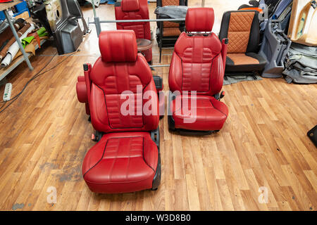 Four sport seats with red leather trim, located on the floor in the workshop for repair and tuning of cars and vehicles Stock Photo