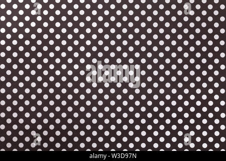 Black background from wrapping paper with a pattern of white polka dot closeup. Texture of silver holiday dotted paper surface. Backdrop of textile. Stock Photo