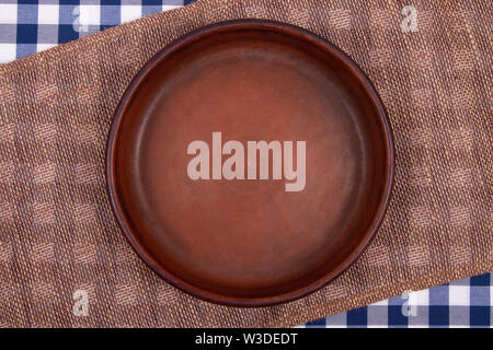 Top view of Empty round clay pan placed on table covered with checkered tablecloth and sacking napkin. Rustic style. Stock Photo