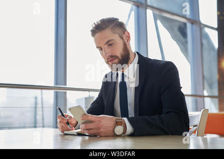 Handsome businessman writing notes from smartphone at modern office Stock Photo