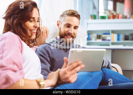 Happy couple sharing digital tablet, sitting on the sofa Stock Photo