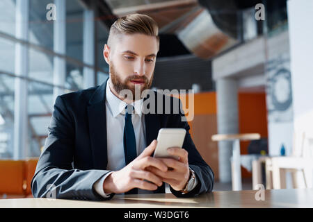 Businessman with beard using his smartphone at modern workplace Stock Photo