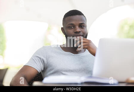 Thoughtful african american guy holding hand near chin in cafe Stock Photo