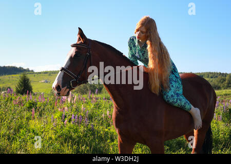 Portrait of young pretty cheerful woman with horse at summer green park Stock Photo
