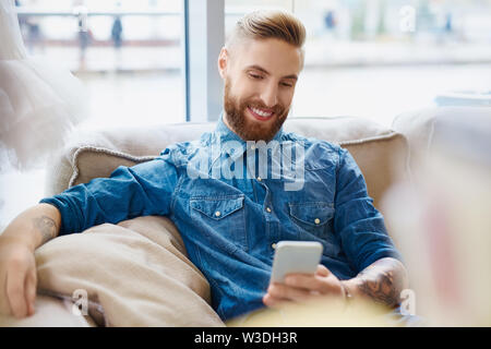 Happy hipster using smart phone at cafe sitting on couch Stock Photo