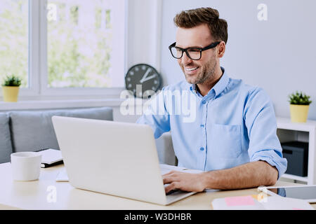 Handsome man using his laptop sitting by table at home Stock Photo