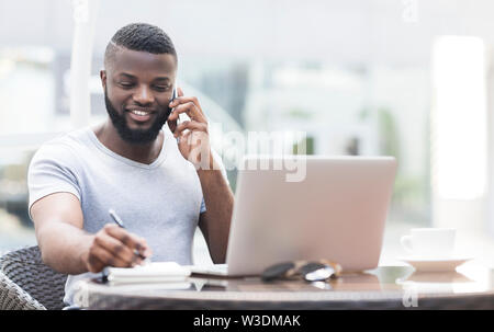 Handsome african american guy speaking on phone and whriting down information Stock Photo