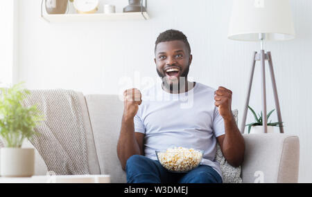 Excited black guy watching sports on tv at home Stock Photo